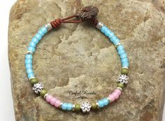 Add a touch of bohemian flair to your outfit with this beautiful minimalist boho beaded leather bracelet. Handcrafted with spring colored seed beads of baby blue, soft pink, and pale olive, interspersed with shimmering silver plated flower beads, this bracelet is sure to add a pop of color to your look. The closure features a decorative coconut button, adding a unique and stylish element to this charming accessory. Perfect for layering or wearing on its own, this bracelet is a versatile and eye- Bohemian Round Beads Bracelets For Spring, Bohemian Spring Bracelets With Round Beads, Adjustable Beaded Bracelets For Spring Festival, Spring Bohemian Adjustable Beaded Bracelets, Bohemian Adjustable Leather Bracelet With Colorful Beads, Adjustable Bohemian Leather Bracelet With Colorful Beads, Bohemian Beaded Bracelets For Beach In Spring, Bohemian Beaded Bracelets For Spring Beach, Bohemian Beaded Bracelets With Tiny Beads For Spring