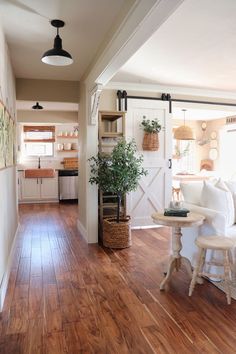 a living room with hard wood flooring and white furniture in the background, an open door leads to a kitchen