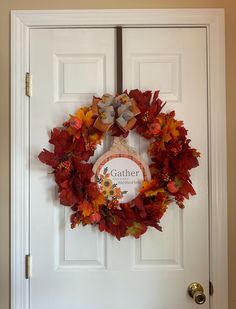 a white door with a wreath hanging on it's side and the words gather surrounded by autumn leaves