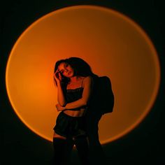 a woman standing in front of an orange circle talking on a cell phone with her arms crossed