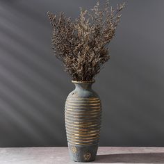 a vase with some plants in it on a table next to a gray wall and grey background