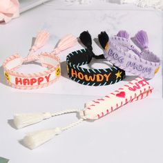 three bracelets with words and tassels on them sitting on a white surface