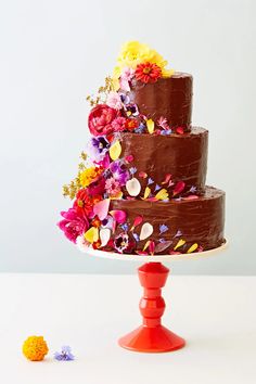 a three tiered chocolate cake with colorful flowers on the top and bottom, sitting on a red pedestal