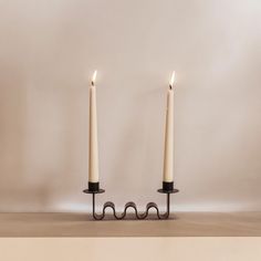 two white candles sitting on top of each other in front of a wall with no one around them