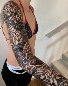 a woman with a tattoo on her arm and chest standing in front of some stairs