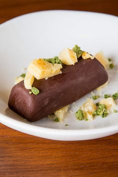 a chocolate dessert on a white plate topped with bananas and green garnishes