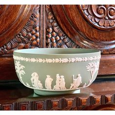 a green bowl sitting on top of a wooden table next to a carved wood panel