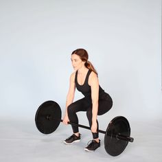 a woman squats with a barbell in front of her on a gray background