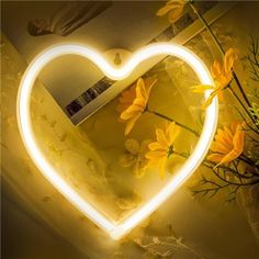 a heart - shaped light up mirror with yellow flowers in the reflection and a vase full of daisies