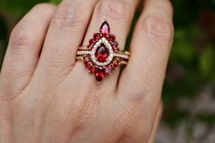 a woman's hand holding a ring with red and white stones on it,