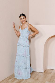 a woman standing in front of a wall wearing a blue dress with ruffles