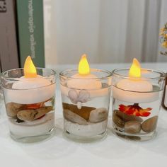 four lit candles sitting on top of rocks in glass vases filled with water and pebbles