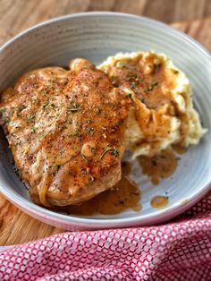 a white bowl filled with meat and mashed potatoes on top of a wooden table