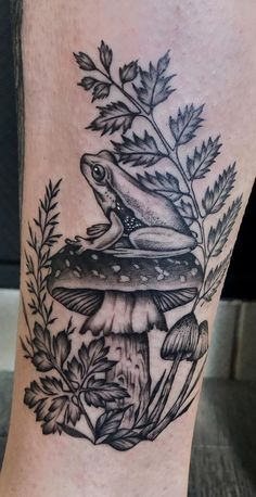 a black and white tattoo of a frog sitting on top of a mushroom with leaves around it