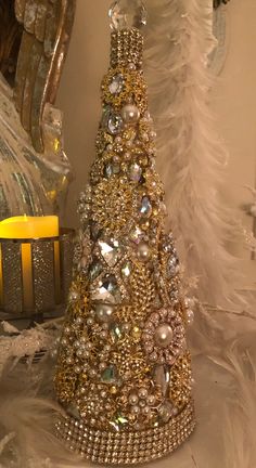 a christmas tree made out of pearls and other jewels sits on a table next to a candle