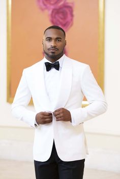 a man in a white tuxedo poses for the camera with his hands on his hips