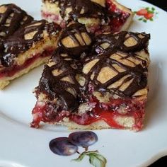 three pieces of dessert on a plate with chocolate drizzled over them and flowers