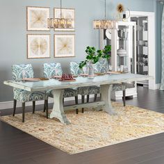 a dining room table with blue chairs and pictures on the wall above it, along with an area rug