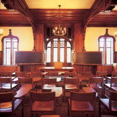 an empty classroom with desks and chairs in front of large windows, along with chandeliers hanging from the ceiling