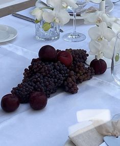 grapes and plums are arranged on a white table cloth at the center of a dining room