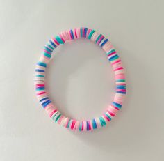 a pink, blue and green striped bracelet on a white surface with a black bead in the middle