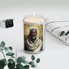 a candle with an image of jesus on it next to some towels and a plant