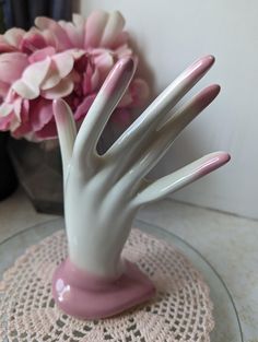 a pink and white hand sculpture sitting on top of a doily