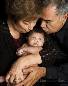 an older man and woman holding a baby in their arms, both looking at the camera