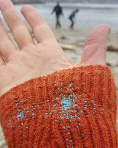 a hand that is wearing an orange knitted mitt with blue dots on it