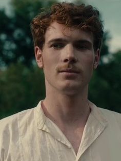 a close up of a person wearing a white shirt and looking at the camera with trees in the background