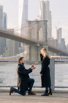 a man kneeling down next to a woman in front of a bridge and the city