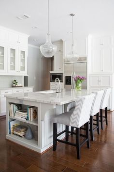 a kitchen with white cabinets and marble counter tops is pictured in this image, there are four bar stools at the center of the island