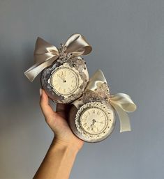 someone holding two clocks in their hand with ribbons on them and bows around the edges