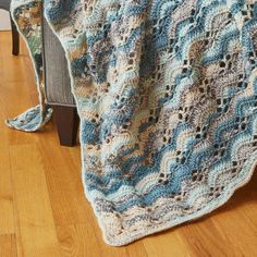 a crocheted blanket sitting on top of a wooden floor next to a chair