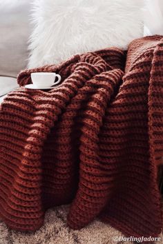 a blanket that is on top of a couch next to a coffee cup and pillow