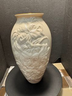 a large white vase sitting on top of a black table next to a tiled floor