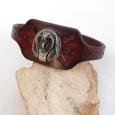 Made from top quality vegetable tanned leather. Hand painted, stamped, antiqued leather cuff bracelet for men. With antique silver Cobra head screw Cobra head sizes: Length; 2.2 cm Width; 2.5 cm  Cuff is 1,33 inches (3,4 cm) wide Sizing (choose at checkout) Please look at my other bracelets! For example this: https://www.etsy.com/listing/253535448/men-leather-cuff-bracelet-tribal-dyed?ref=shop_home_active_1 FEDEX to USA, Canada and Australia! If you need a faster shipping please use this service Vintage Leather Bracelet With Engraving, Vintage Engraved Leather Bracelets, Vintage Leather Engraved Bracelet, Vintage Brown Engraved Cuff Bracelet, Vintage Brown Engraved Bracelets, Adjustable Carved Cuff Bangle, Cobra Head, Bracelet Indian, Leather Cuff Bracelet