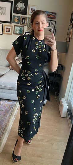 a woman taking a selfie in her living room wearing a black floral print dress