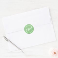 a white envelope with a green sticker on it next to a pen and flower