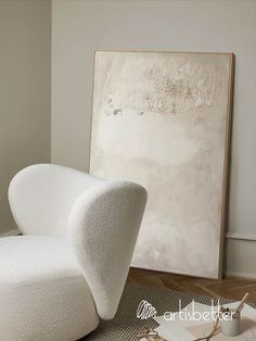 a white chair sitting on top of a wooden floor next to a large piece of art