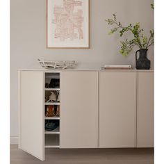 a white cabinet with open doors next to a plant in a vase and pictures on the wall