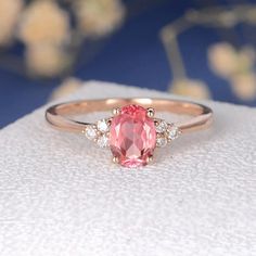 a pink ring with three diamonds on it sitting on top of a white cloth next to flowers