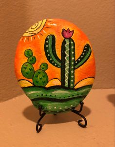 a painted rock sitting on top of a table next to a vase filled with flowers and cacti