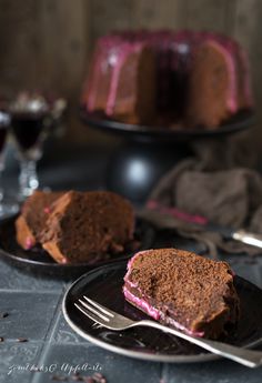 two slices of chocolate cake on black plates with silverware and wine glasses in the background