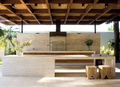 an outdoor kitchen and dining area with wood beams on the ceiling, surrounded by palm trees