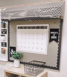 a desk with a calendar and some baskets on top of it, in front of a white wall