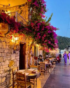 people are walking down the sidewalk in front of an outdoor restaurant with flowers hanging over it