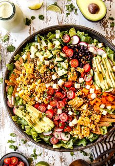 a large salad with corn, tomatoes, avocado and other vegetables on it