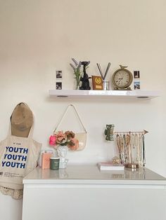 a white counter topped with lots of items next to a clock and vase filled with flowers