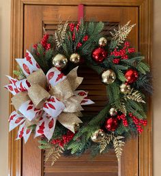 a christmas wreath on a door with red and gold ornaments hanging from it's side